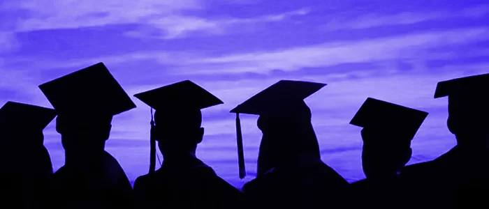 Silhouettes of graduates in Caps and Gowns in front of a dark blue sky
